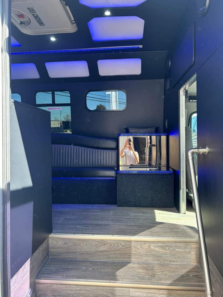 Interior of a Limo Bus with blue lights, person’s reflection in mirror near black seats.