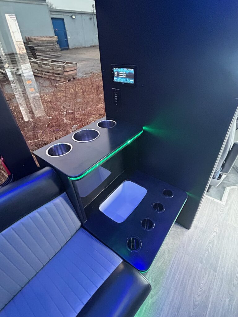 Modern limo bus interior with cup holders, touchscreen, and open cooler—ideal for bachelor parties.