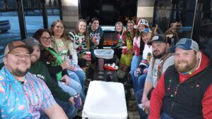 Thirteen people in festive outfits enjoy drinks and a fake fireplace on an Xtreme Party Bus.