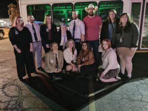 Thirteen people pose at night by a Limo Bus, some kneeling and others standing in celebration.