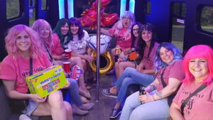 Women in colorful wigs and pink shirts enjoy snacks on a Wisconsin Xtreme Party Bus Service ride.