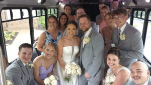 Wedding party in formal wear smiles on a Wisconsin Limo Bus, holding flowers and posing together.