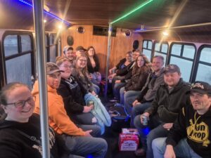 A group of friends sit smiling on a Wisconsin limo bus with drinks and snacks between them.