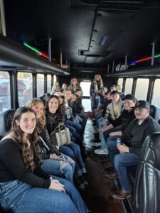 A group of people sit smiling inside a Wisconsin bachelor party bus with colorful lights above.