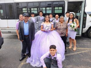 A girl in a purple ball gown and her group pose outdoors by a Wedding Shuttle bus.