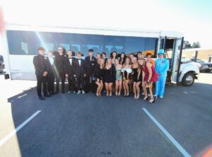 A group of teens in formalwear pose by a white party bus, ready for a Wisconsin Wedding Shuttle.