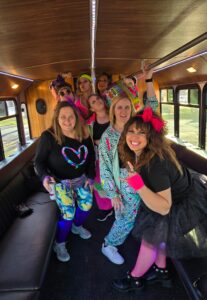 Group of women in colorful 80s outfits smile on a party bus during a Wisconsin bachelorette party.