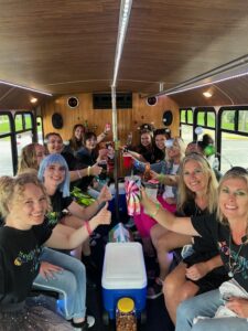 A group of women on a Limo Bus, smiling and holding drinks, enjoying a fun bachelorette party.