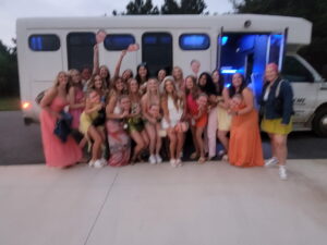 A group smiles in front of an Xtreme Party Bus Service ride on a Wisconsin driveway at dusk.
