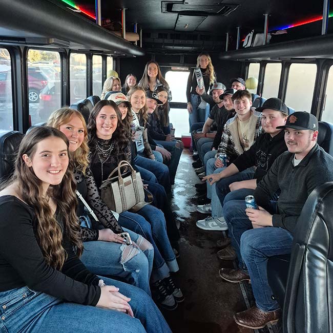 Young adults smile inside an Xtreme Party Bus Service limo bus, facing each other in two rows.