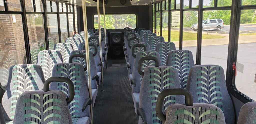 Rows of empty patterned limo bus seats with bright daylight streaming through the windows.