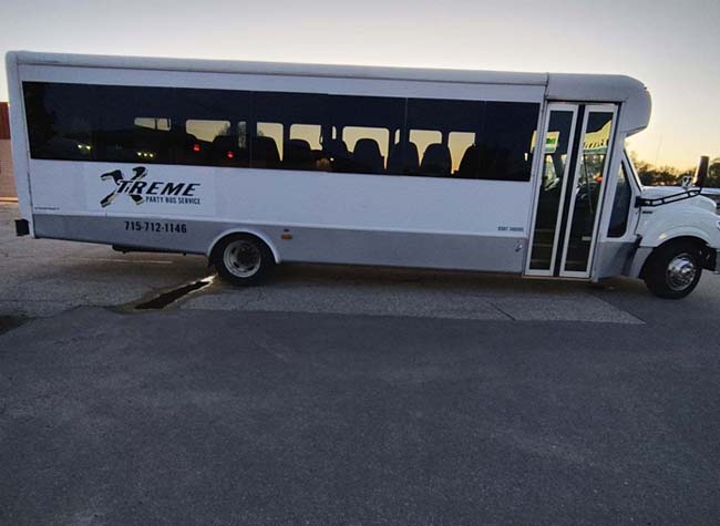 A white Wedding Shuttle bus parked with its back wheels on a curb, causing it to tilt backward.