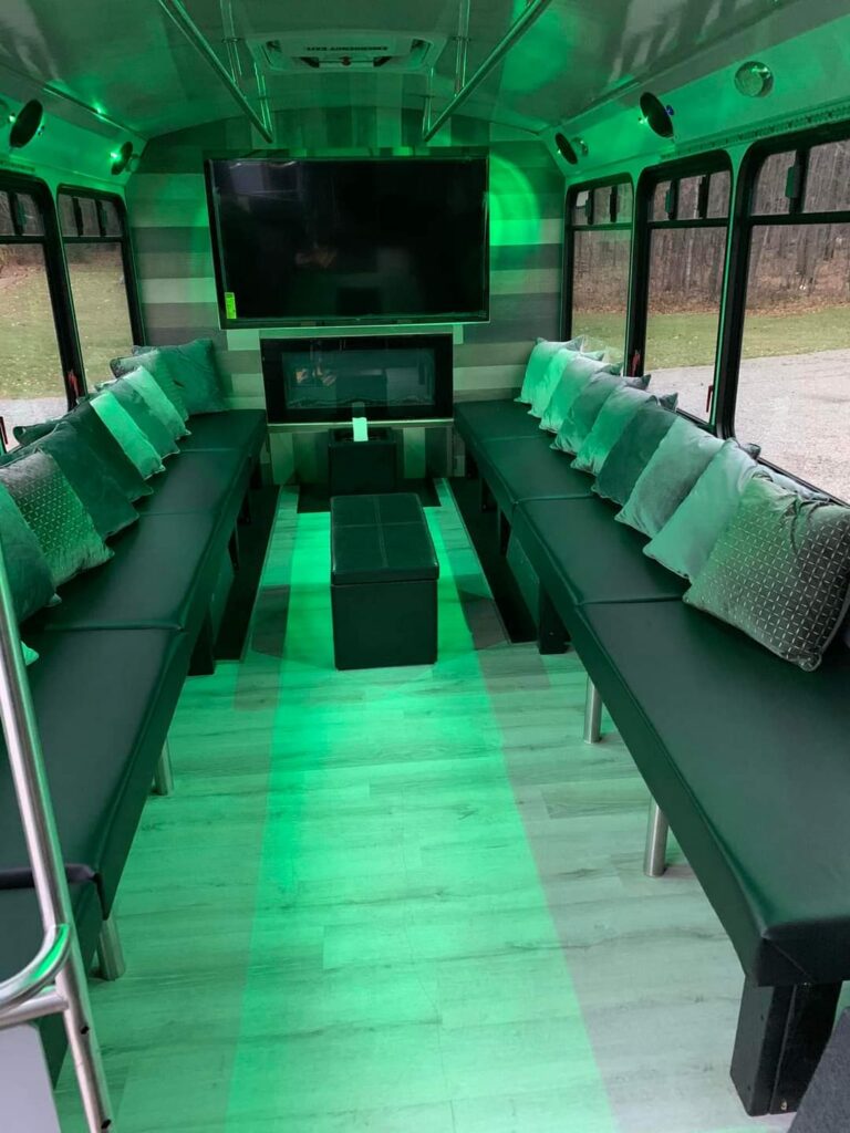 Limo Bus interior with black benches, green lighting, TV, pillows, and faux fireplace in Wisconsin.