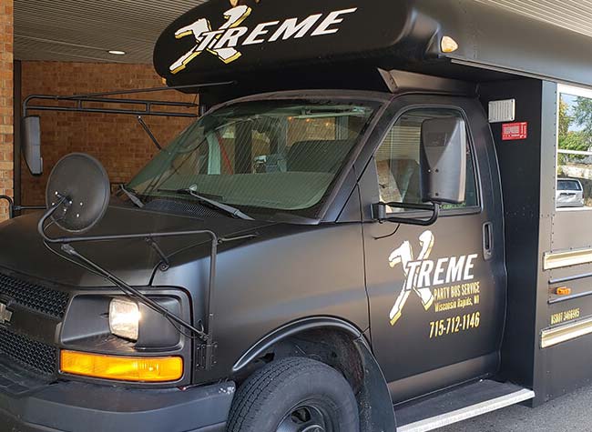 Black Xtreme Party Bus for Bachelor/Bachelorette Party parked beside a brick building.