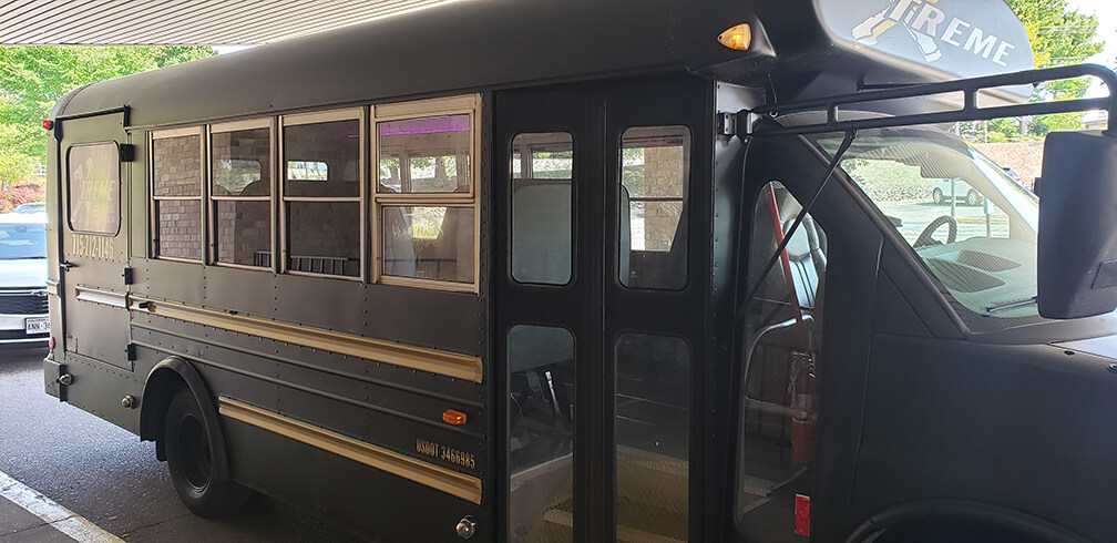 A black Limo Bus with open door is parked by a curb, showing windows and driver's area.