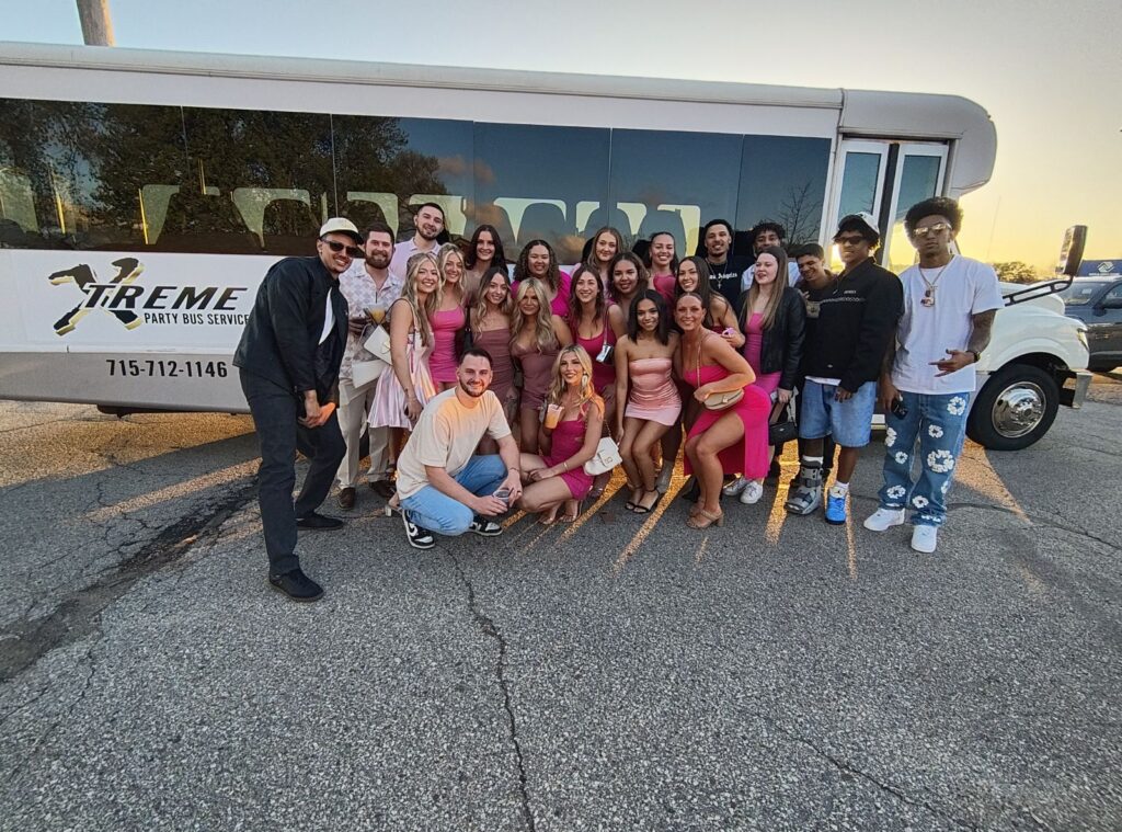 Group of young adults in vibrant outfits posing by a Limo Bus for a Wisconsin bachelorette party.
