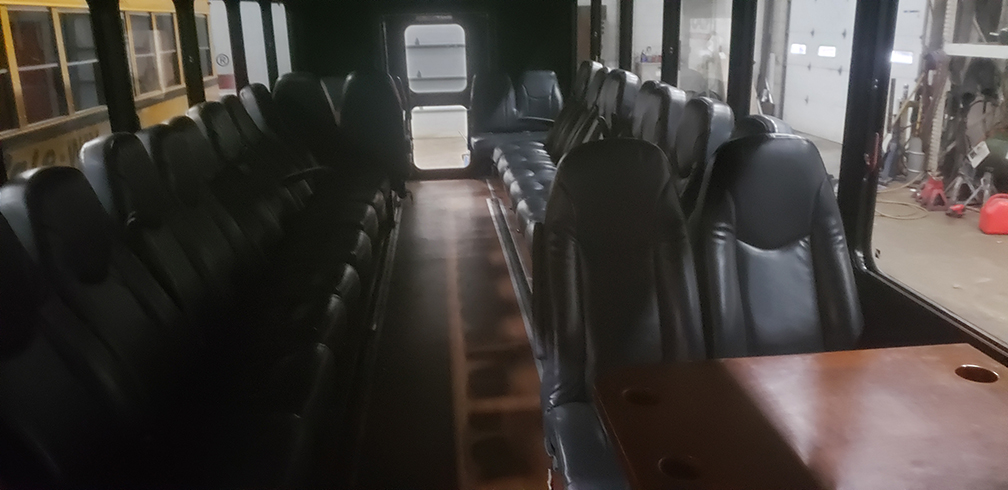 Limo Bus interior with rows of black leather seats and a small table, seen from the front.